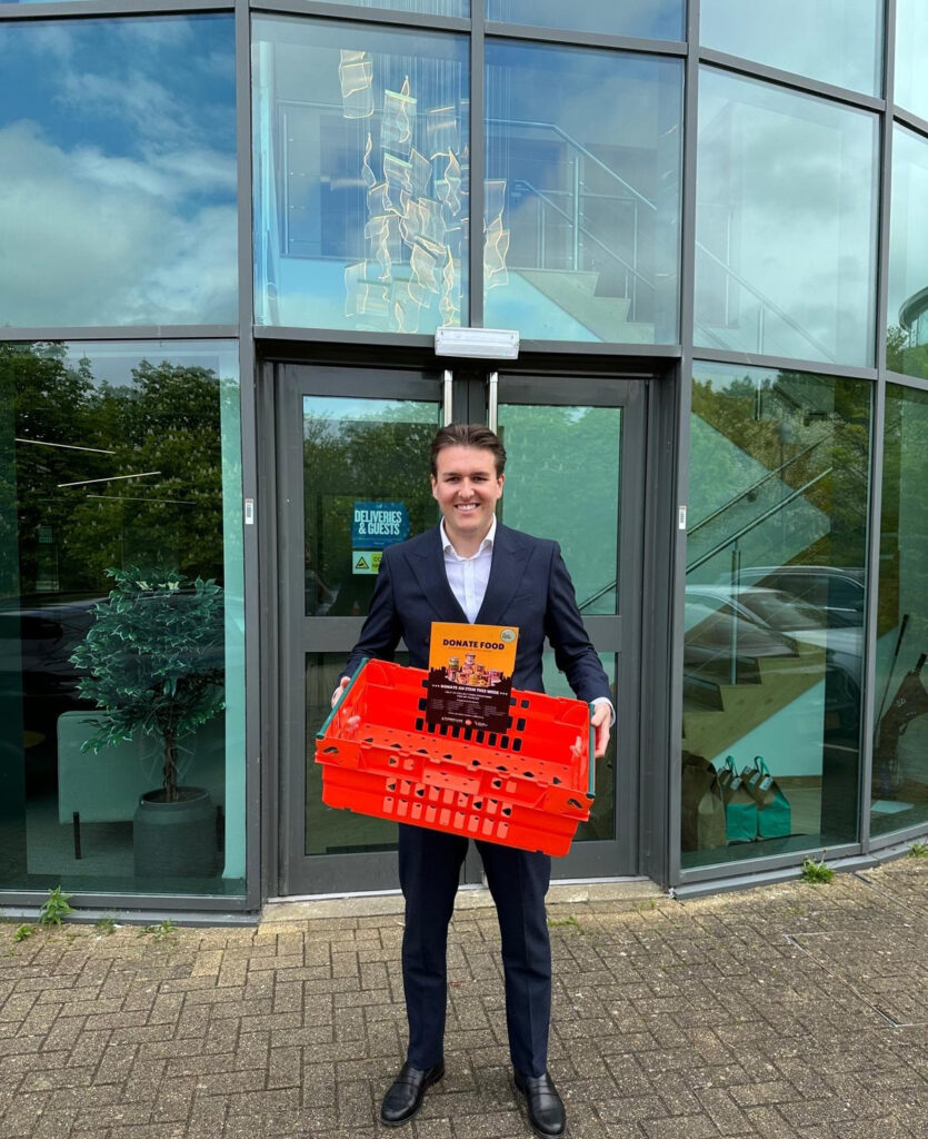 Crown Business Finance team member holding MK Food Bank donation crate outside office in Milton Keynes