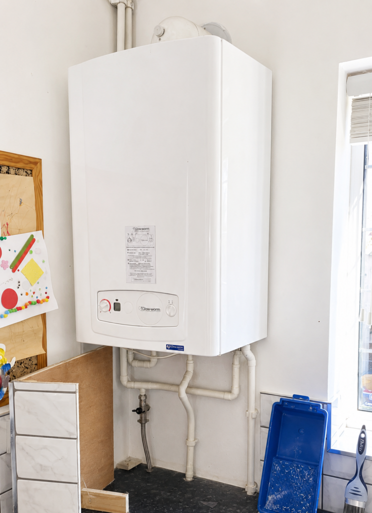 Domestic wall-mounted Glow-worm boiler installed in a residential kitchen showing heating system pipework and boiler unit used for home heating and hot water in Milton Keynes.