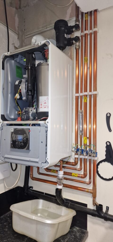 Domestic boiler repair and servicing work in progress showing opened condensing boiler, magnetic system filter, copper pipework and heating system maintenance setup in a residential property in Milton Keynes