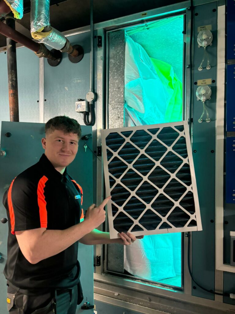 engineer holding an air filter beside an air handling unit